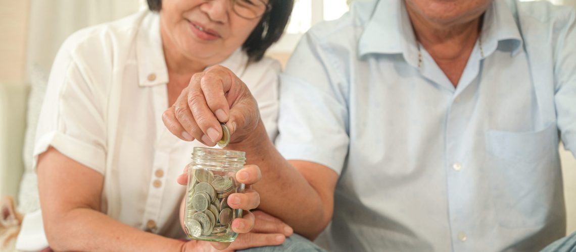 Old asian women and men sit on the sofa, they make financial plans.An old man pretending to hold a coin in a glass bottle,They smile happily.