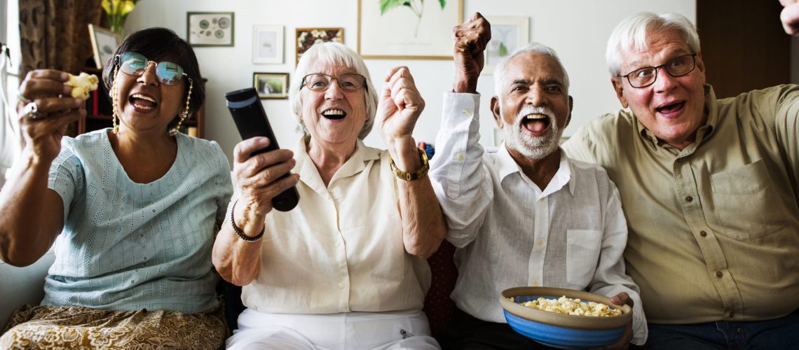 Group of cheerful senior friends sitting and watching TV together