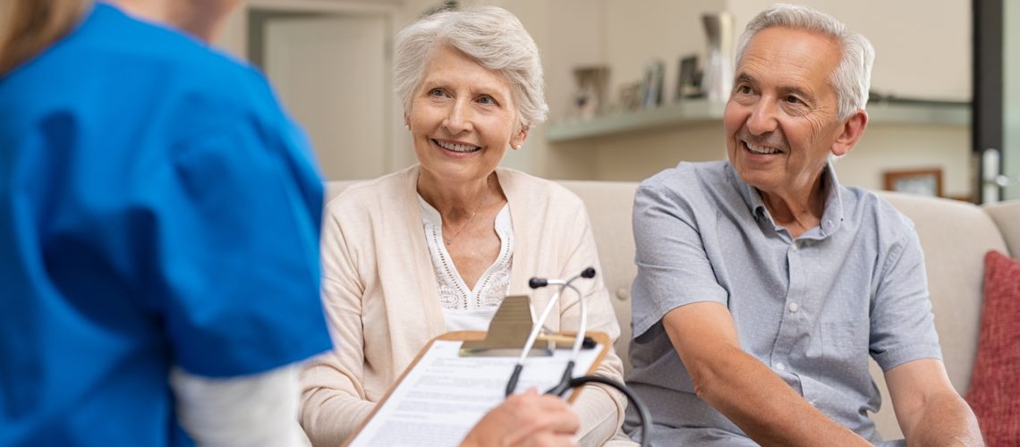 Nurse during home visit with senior couple. Doctor holding clipboard and stethoscope in conversation with old couple at home. Nurse bringing home the results of medical exams.