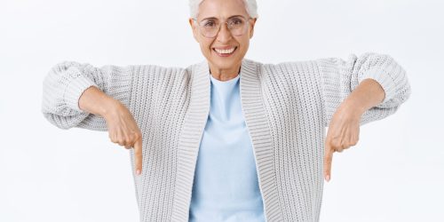 Satisfied, confident, glad, smiling happy senior woman with grey hair, in glasses, pointing down to turn attention awesome promo sale, showing her enthusiasm, recommend advertisement, click on banner.