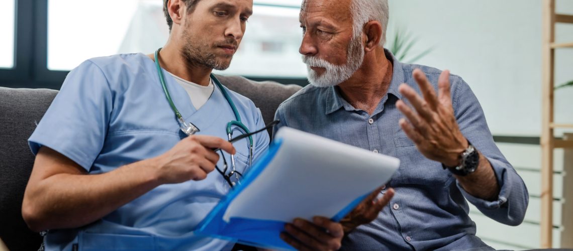 Senior man talking to a doctor who is reading medical test results while being in a home visit.